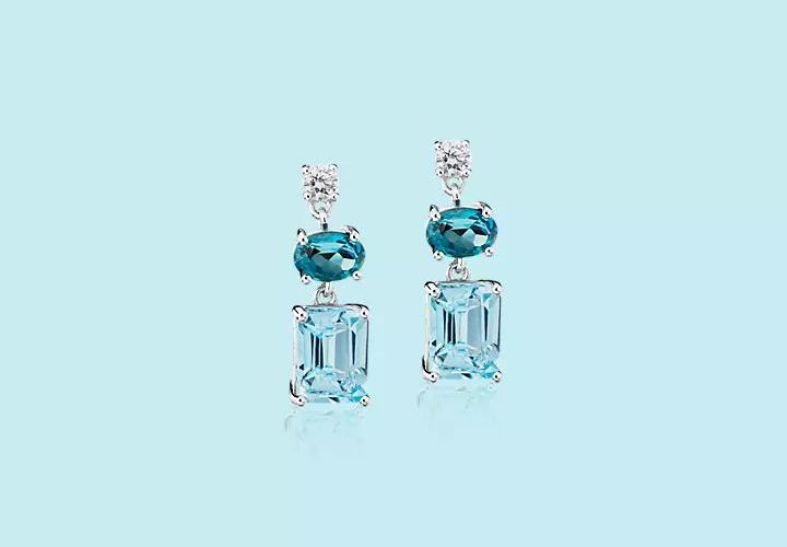 Blue topaz gemstones in oval and emerald cuts featured in a pair of earrings